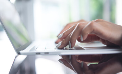 Wall Mural - Woman hand typing on laptop computer keyboard on white office table, close up. Business woman online working on laptop computer at home office, online job, surfing the internet, remote work