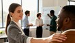 © ubay - A woman places her hand on a man's shoulder in a bright office setting with colleagues working in the background.