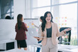 © MINAE - Asian businesswoman smiling and holding a laptop, leading a professional meeting or business presentation while colleagues collaborate in a modern office setup