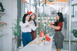 © MINAE - Three young Asian women wearing festive headwear are happily dancing and smiling during a Christmas celebration or holiday party in a modern office environment