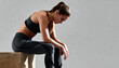 © NanieStudio - Fit athletic woman in workout clothes resting after exercise training session, exhausted fitness model in gray sportswear taking break sitting on wooden box, sports recovery and fatigue concept