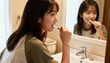 © Miriam - Young Asian woman brushing teeth with a toothbrush in the bathroom. Morning routine, oral hygiene, and dental care. Healthy lifestyle and self-care concept for fresh breath and clean teeth.