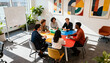 © Hannah - Diverse creative business team in a meeting. Multi-ethnic colleagues collaborating on a project, brainstorming ideas in a modern, sunny office with a colorful table and whiteboard.
