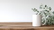 © minang - A minimalist mockup of a blank white mug on a wooden surface, surrounded by soft eucalyptus foliage against a clean white wall.