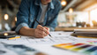 © Lara - Person drawing architectural plans on desk with color swatches