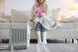 © New Africa - Young woman on sofa near electric heater at home, selective focus