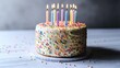 © tangguo - Simple Warm Birthday Cake Close-up: Colorful Sprinkles & Candles on Centered White Background Empty Table, Contrasting Grey Floor, Clean Festive Atmosphere
