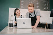 © BigBlues - Two baristas, a man and a woman in black aprons, work together behind counter. The man is looking at a laptop, and the woman is checking a tablet while standing next to a couple of to-go coffee cups.