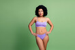 © deagreez - Attractive young woman in purple underwear posing against vibrant green background embodying body positivity