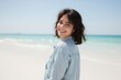 © HasnainRaza - A person with wavy, shoulder-length hair stands on a pristine beach, wearing a light blue shirt, with the turquoise ocean and clear blue sky stretching out in the background.