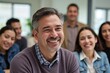 © Abdullah - Close-up portrait of a Hispanic man laughing joyfully in a business-casual office meeting with diverse colleagues, candid authentic moment