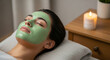 © haris - Woman relaxing with a green facial mask, eyes closed, lying on a pillow next to a lit candle and plant.