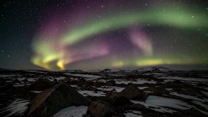 Wall Mural - glowing aurora borealis ribboning over barren rocky landscape under a darkened arctic sky timelapse 