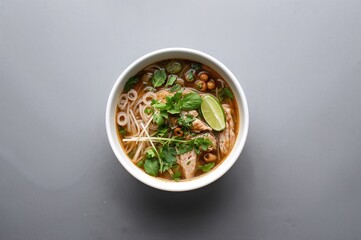 Wall Mural - Traditional chicken noodle soup served with fresh herbs and vegetables in a bowl on a gray surface. Asian dish with space for text.