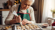 © Anisgott - Happy senior woman in green apron carefully decorating gingerbread cookies with white icing on tray in cozy Christmas kitchen with festive details
