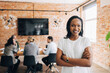 © Maskot - Portrait of smiling young female business expert standing with arms crossed in office
