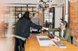 © Maskot - Happy woman shaking hands with male recruiter sitting at table for job interview in office