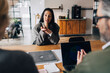 © Maskot - Woman gesturing while giving interview to business experts while sitting at table in office