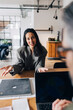© Maskot - Woman gesturing while answering questions during interview with business experts while sitting at table in office