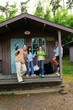 © Maskot - Portrait of smiling kids gesturing while standing with female camp counselor on porch of log cabin