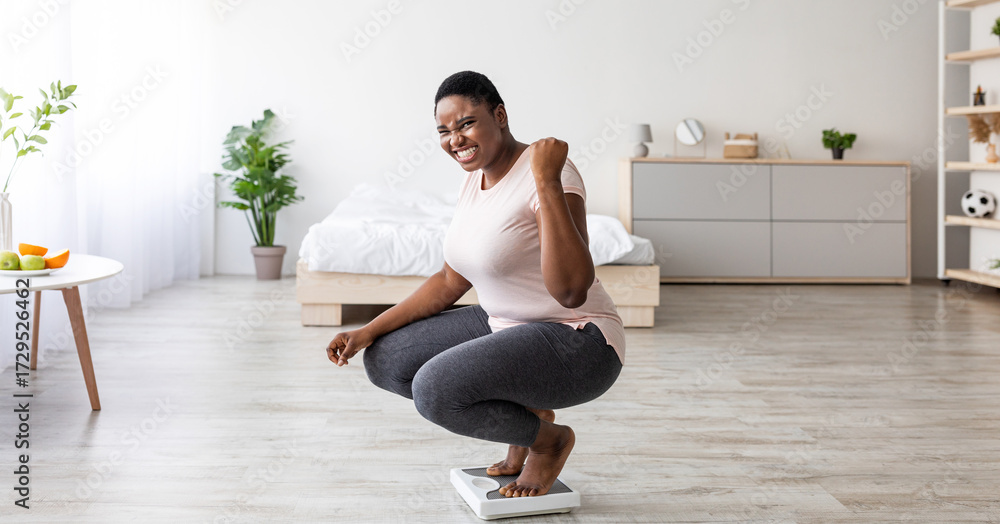 Excited curvy black woman sitting on scales at home, making YES gesture ...