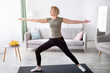 © Prostock-studio - Strength yoga exercises. Fit mature lady standing in warrior asana, exercising on sports mat at home. Fit senior woman doing domestic workout, practicing pilates during coronavirus lockdown
