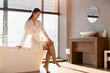 © Prostock-studio - Sensual attractive young korean woman in white bathrobe sitting on bathtub, touching her legs, enjoying silky, smooth, hairless skin, bathroom interior, sun flare, panorama with copy space
