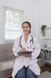 © SOMKID - Female doctor preparing for or documenting a check-up, Smiling female doctor, Professional physician in a modern office.