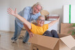 © luciano - A playful older couple moves into a new home, surrounded by moving boxes in an empty room. A concept of a fresh start, retirement, and relocation.