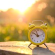 © Erika - Yellow alarm clock on wooden surface, sunlit background