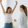 © Elzayady - Woman celebrating weight loss success with arms raised as doctor looks on with a measuring tape around waist