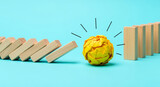 Wooden dominoes falling towards yellow paper ball on blue surface, suggesting disruption and new idea, representing influence, obstacle, potential impact