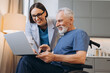 © Maria Vitkovska - Caregiver assisting senior man in wheelchair using laptop