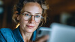 © raseldesigner93 - Woman with freckles wearing glasses smiling while looking at a smartphone with a laptop nearby happy