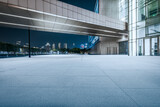 Empty stone ground of an outdoor plaza in front of a modern office building with the city skyline at night.
