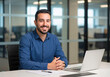 © InfinityVisuals - Cheerful Professional at Work: A confident man sits at a sleek office desk, radiating positivity.