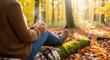 © remake - Woman sitting on forest ground holding steaming coffee cup wrapped in plaid blanket. Cozy autumn moment with warm drink among golden fall leaves and trees in peaceful woodland setting.