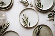 © Sergey - A serene flat lay composition featuring rustic ceramic plates adorned with fresh olive branches and a warm candle glow.