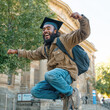 © valeo5 - Excited young man in casual attire, a black graduation cap, backpack, captured mid-air jump with wide, smile, raised fists, celebrating his university graduation in front of classic campus building