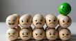 © Aimo Studio - Green happy face stands out among wooden balls with sad and angry expressions on a neutral background
