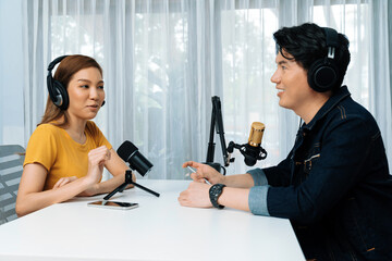 Smiling radio influencer host wearing headphone interviewing woman speaker sharing information to listeners on social media online website live streaming channel at morning at studio record. Infobahn.
