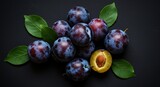 Fresh plums with green leaves against a dark background
