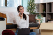 © itchaznong - Remote Work. Young woman on phone while unpacking in new apartment.