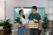 © itchaznong - Couple Collaborating: Young Partners Carrying Plants and Boxes in New Home