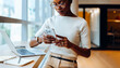 © (JLco) Julia Amaral - Businesswoman reading her smartphone while working on her laptop at a desk