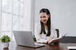 © amnaj - Asian woman reading book at home office desk