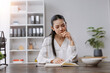 © amnaj - Asian woman reading book eating snack in office