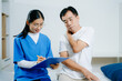 © Nuttapong punna - Young female nurse assists elderly man with neck pain. Ideal for healthcare, pain management, physiotherapy, nursing, and senior medical consultation stock themes.