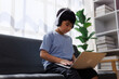 © Phimwilai - Asian boy using laptop wearing headphones at home