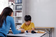 © Phimwilai - Asian teacher helping young student doing homework in classroom